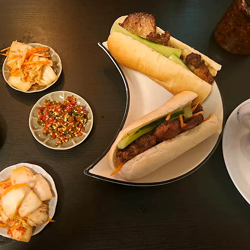 Kaksi bánh mì -patonkia grillatulla porsaalla, vieressä pikkelöityjä kasviksia ja chiliä