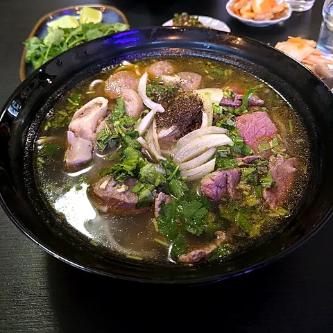 Bún Bò Huế -keitto valkoisessa kulhossa, päällä sipulia, kevätsipulia ja korianteria
