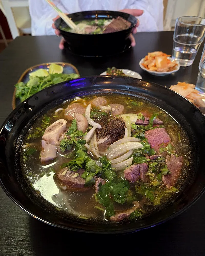 Iso phở-kulho pöydällä, taustalla lisukkeita ja vesilasit